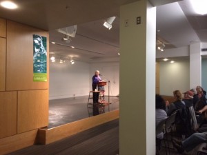 An image of Sally Woolf-Wade reading a poem out loud in front of an audience.