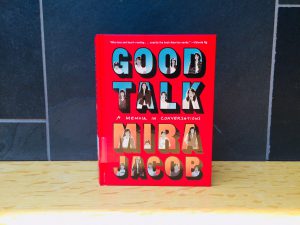 A picture of the book Good Talk by Mira Jacob. It is a red book with illustrations on the cover depicting the author as a child, teenager, and adult. 