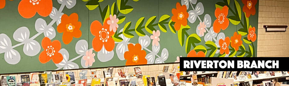 A view of the Riverton Branch with the bookshelves in the foreground and the Rachel Adams in the background.