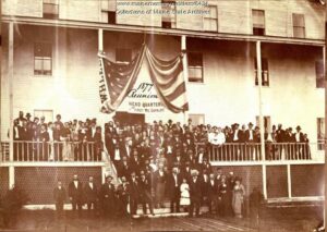 A photo from 1877 depicting a group of people gathered along the porch of a building in Old Orchard Beach, Maine. Among the many people gathered is Frederick Douglass.