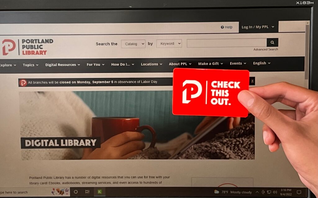 A library card holder holds their card in front of a computer screen displaying the "Digital Library" page on PPL's website.