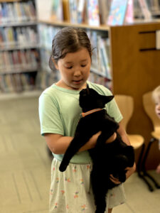A young girl holds a black cat in the children's library during a Summer Reading event.