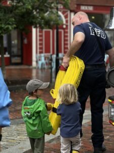 A Portland Fire Department firefighter shows two young children a bright yellow fire hose