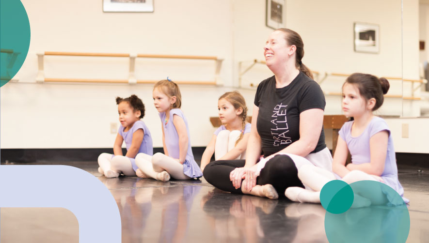 Four children sit with a ballet instructor at a pre-ballet class